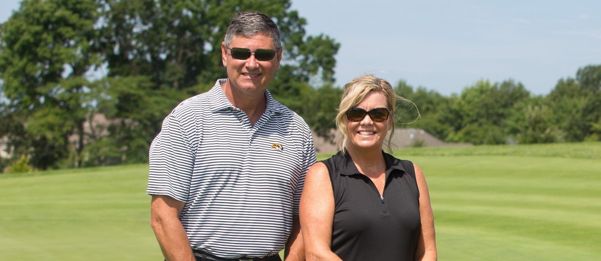 man and his wife standing on a golf course smiling at the camera