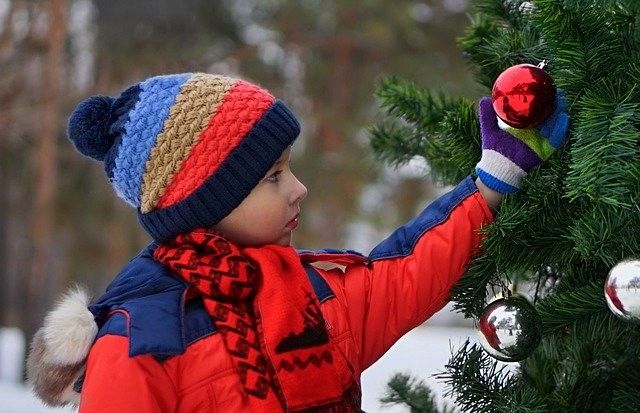 child touching ornament on outdoor christmas tree in snow wearing red coat and scarf