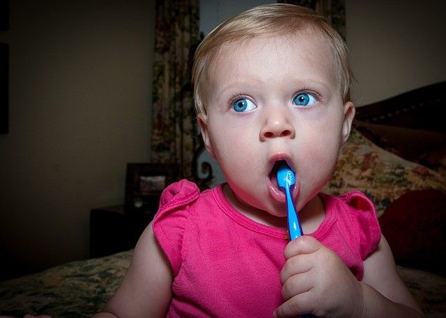 child with pink shirt holing mouth open with a toothbrush in their mouth